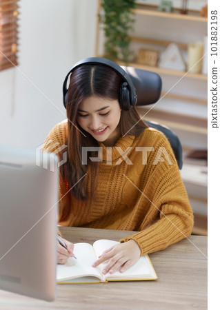Online education, e-learning. Asian woman in stylish casual clothes, studying using a computer, listening to online lecture, taking notes, online study at home 101882198