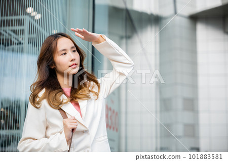 Portrait of confidence young businesswoman standing outside office building in city raise her hand to shade sun UV. Happy woman wearing white suit jacket with brown bag at sunlight outdoors. sun block Portrait of confidence young businesswoman standing outside office building in city raise her hand to shade sun UV. Happy woman wearing white suit jacket with brown bag at sunlight outdoors. sun block 101883581