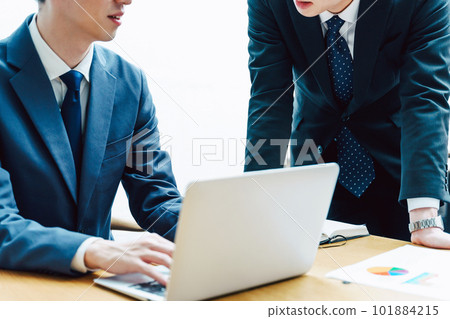 Two faceless men in suits discussing business with their colleagues and boss at their desks while working on their laptops Two faceless men in suits discussing business with their colleagues and boss at their desks while working on their laptops 101884215