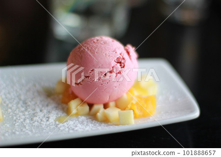 A ball of pink ice cream on a white plate with pieces of fruit A ball of pink ice cream on a white plate with pieces of fruit 101888657