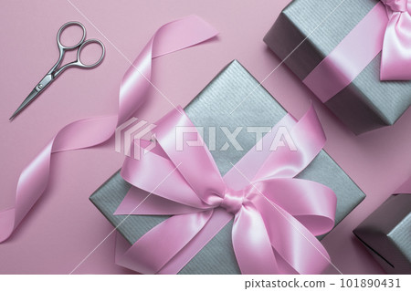 Silver gray gift boxes with pink satin bows and wrapping materials on pink background. Gift wrapping idea. 101890431