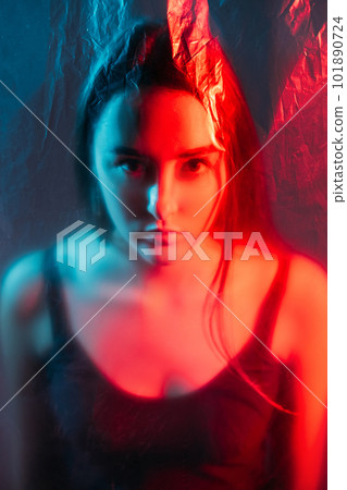 Bipolar disorder. Split personality. Mental crisis. Red blue color light defocused art portrait of serious woman face behind distressed transparent polyethylene plastic film wall. Bipolar disorder. Split personality. Mental crisis. Red blue color light defocused art portrait of serious woman face behind distressed transparent polyethylene plastic film wall. 101890724