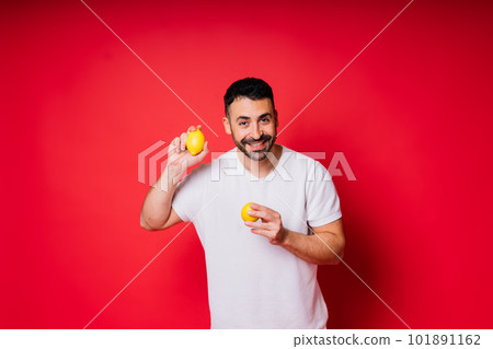 Portrait of young bearded man holding lemons in both hands on isolated red background Portrait of young bearded man holding lemons in both hands on isolated red background 101891162