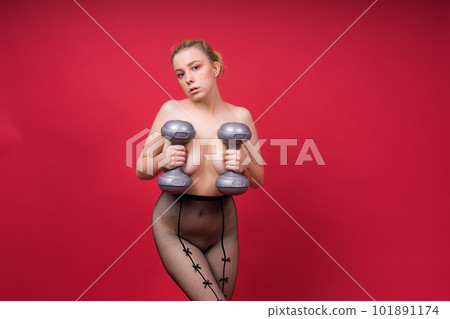 Beautiful model in sportswear with dumbbells looks at the camera on yellow, red and dark background 101891174