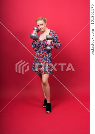 Beautiful model in sportswear with dumbbells looks at the camera on yellow, red and dark background 101891179