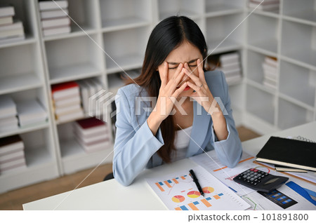 Tired Asian businesswoman sits at her desk, suffering from eye strain. Tired Asian businesswoman sits at her desk, suffering from eye strain. 101891800