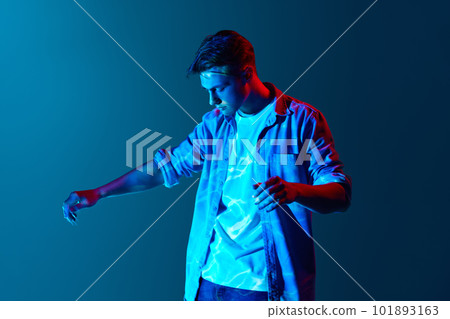 Young man standing with digital neon lights reflection on face and body over blue background. Fantasy and futurism Young man standing with digital neon lights reflection on face and body over blue background. Fantasy and futurism 101893163