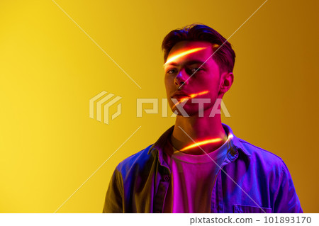 Handsome young man in casual stylish clothes with digital neon filter reflection on face standing against gradient yellow background Handsome young man in casual stylish clothes with digital neon filter reflection on face standing against gradient yellow background 101893170