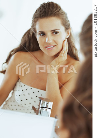 Happy young woman checking facial skin condition in bathroom 101893217