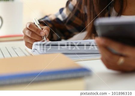 Woman writes hand on agenda while consulting mobile phone on desk at home or in office 101896310