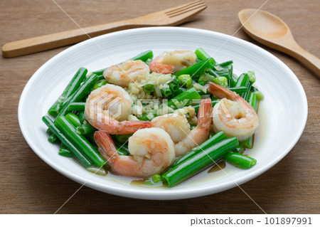 close up of stir fried shrimp with onion flower stem in a ceramic dish on wooden table. asian homemade style food concept. close up of stir fried shrimp with onion flower stem in a ceramic dish on wooden table. asian homemade style food concept. 101897991