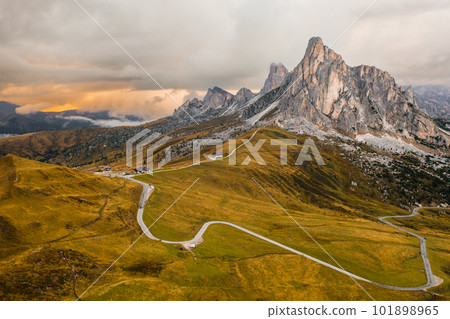 Pathway from Snake Road to high mountain range illuminated by bright sunlight. Small mountain resort for tourists located in Giau Pass Pathway from Snake Road to high mountain range illuminated by bright sunlight. Small mountain resort for tourists located in Giau Pass 101898965