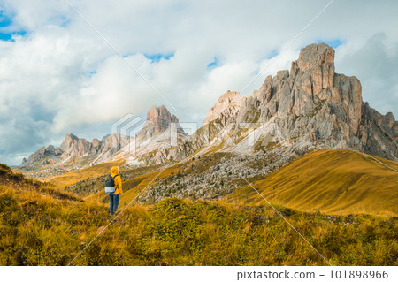 Tourist in yellow jacket and backpack enjoying the exploration amidst the towering mountains of the famous Giau Pass.  101898966