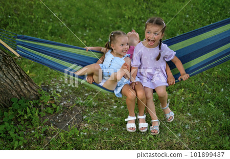 Comical humorous children laugh merrily while swinging on a hammock in the park. Children's recreation and entertainment during the summer holidays Comical humorous children laugh merrily while swinging on a hammock in the park. Children's recreation and entertainment during the summer holidays 101899487
