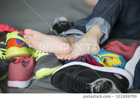 Bare feet in a pile of shoes. Children's foot on the background of sneakers. Foot and shoes Bare feet in a pile of shoes. Children's foot on the background of sneakers. Foot and shoes 101899709