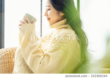 Portrait of a woman wearing a knitted sweater drinking coffee leisurely 101900164