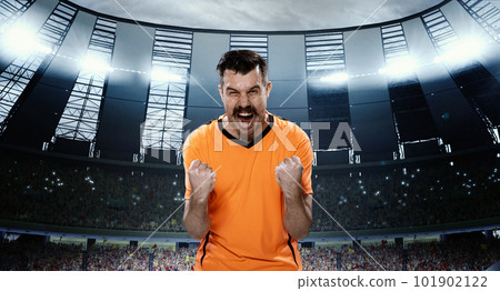 Growing winning spirit before game. Emotional man, professional football sportsman in orange uniform standing on 3D field with spotlights 101902122