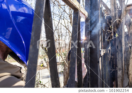 welder welds hinge on gate with welding electrode welder welds hinge on gate with welding electrode 101902254