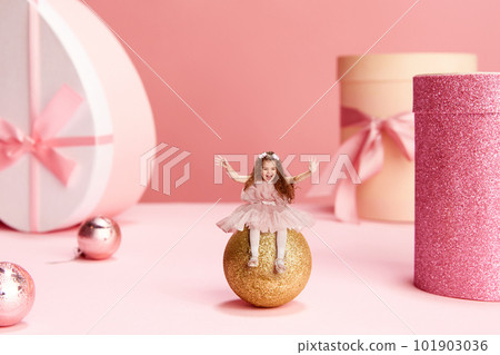 Merry Christmas and Happy new year. Happy, smiling, little girl, child in cute dress sitting on decorations and having fun over pink background Merry Christmas and Happy new year. Happy, smiling, little girl, child in cute dress sitting on decorations and having fun over pink background 101903036