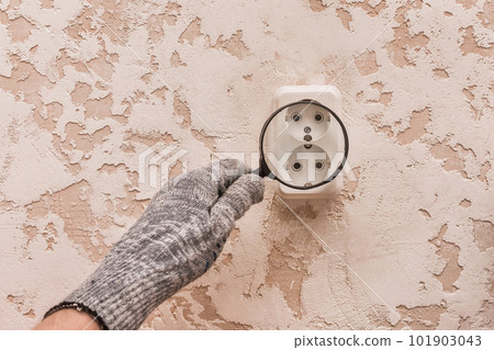 The hand of a male construction worker in protective gloves examines through a magnifying glass the connection of appliances The hand of a male construction worker in protective gloves examines through a magnifying glass the connection of appliances 101903043