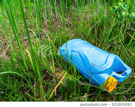 A blue plastic canister in a junkyard in the green grass. A blue plastic canister in a junkyard in the green grass. 101905093