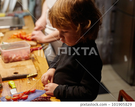 A little boy works in the kitchen, he cuts a tomatoes 101905829