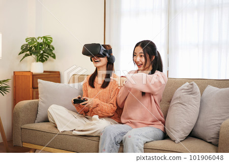 Young woman lesbian couple wearing sweater and VR goggles while Young woman lesbian couple wearing sweater and VR goggles while 101906048