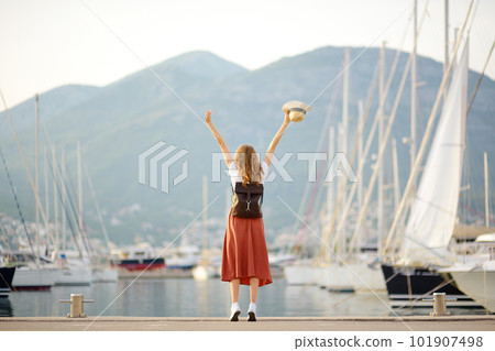 Charming young woman meets someone from a voyage on the Mediterranean sea. An attractive red-haired tourist girl against the background of the sea and yachts. Yacht rental. Freedom and vacation Charming young woman meets someone from a voyage on the Mediterranean sea. An attractive red-haired tourist girl against the background of the sea and yachts. Yacht rental. Freedom and vacation 101907498