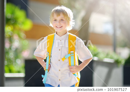 Little schoolboy joyfully goes to school after holiday. Child in a yard of schoolhouse. Quality education for children. Kids back to school Little schoolboy joyfully goes to school after holiday. Child in a yard of schoolhouse. Quality education for children. Kids back to school 101907527