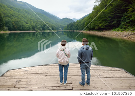 Tourists admiring of breathtaking landscape of mountain lake Biogradsko in alps of Montenegro on spring day. Stunning view of mountains and valleys in national park Biogradska Gora. Tourists admiring of breathtaking landscape of mountain lake Biogradsko in alps of Montenegro on spring day. Stunning view of mountains and valleys in national park Biogradska Gora. 101907550