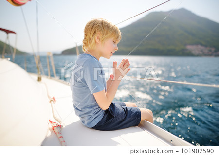 Little boy on board a sailing boat in the Boka Kotor Bay of the Adriatic Sea in the Balkan Mountains, Montenegro, Europe. Happy child on a sea trip during the sunny summer holidays day. Little boy on board a sailing boat in the Boka Kotor Bay of the Adriatic Sea in the Balkan Mountains, Montenegro, Europe. Happy child on a sea trip during the sunny summer holidays day. 101907590