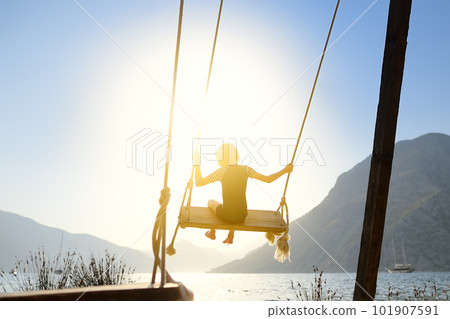 Little boy having fun on large swing on the shore in the Boka Kotor Bay of the Adriatic Sea in the Balkan Mountains, Montenegro. Happy child on a sea resort on sunny summer holidays day. Little boy having fun on large swing on the shore in the Boka Kotor Bay of the Adriatic Sea in the Balkan Mountains, Montenegro. Happy child on a sea resort on sunny summer holidays day. 101907591