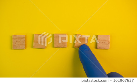 Hand in blue gloves point on clean wooden blocks on colored yellow background. Medical scientific or biological theme. Template for text or concept. Advertising mock up. Presentation flat lay mock up Hand in blue gloves point on clean wooden blocks on colored yellow background. Medical scientific or biological theme. Template for text or concept. Advertising mock up. Presentation flat lay mock up 101907637
