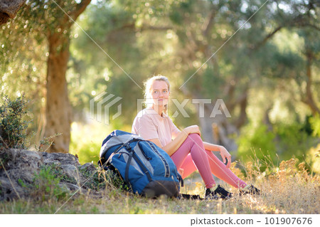 Young woman hiking in countryside. Girl resting under olive tree. Concepts of adventure, extreme survival, orienteering. Backpacking hike Young woman hiking in countryside. Girl resting under olive tree. Concepts of adventure, extreme survival, orienteering. Backpacking hike 101907676