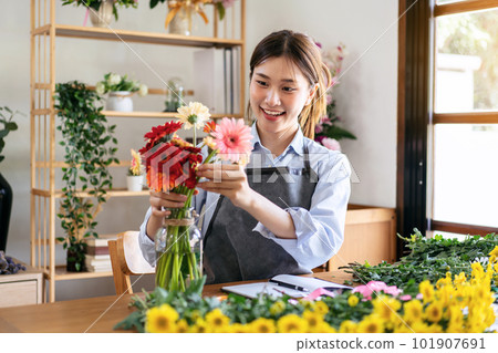 Female florist in apron smiling and arranging gerbera flowers in 101907691