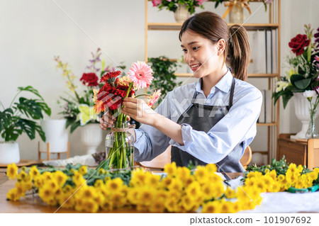 Female florist in apron smiling and arranging gerbera flowers in Female florist in apron smiling and arranging gerbera flowers in 101907692