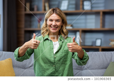 Portrait of a happy senior woman in a green dress sitting on the couch at home and smiling and showing super hands to the camera. Portrait of a happy senior woman in a green dress sitting on the couch at home and smiling and showing super hands to the camera. 101908365