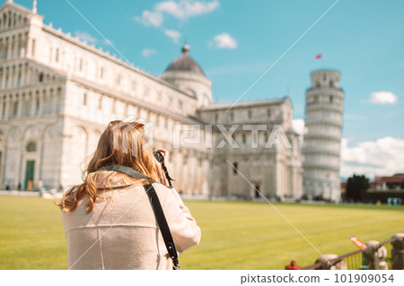 Back view of blonde woman with a camera taking pictures of the Leaning Tower of Pisa on a sunny, clear day. 101909054