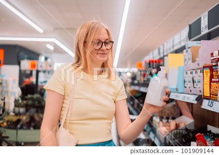 Young cheerful smiling woman chooses a bottle of liquid soap in a supermarket  101909144