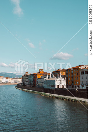 A beautiful view of buildings along the Arno river in Pisa, Italy. A bridge passes over the river and houses on both sides are overlooking the water 101909342