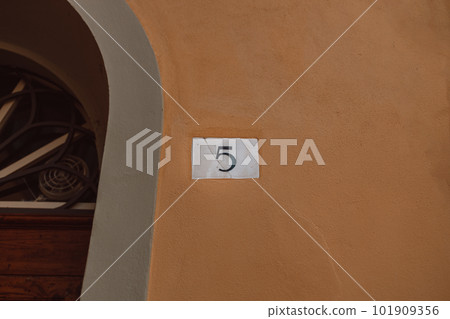 Ceramic house number five 5 house number on orange wall background.  101909356
