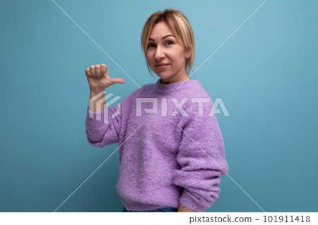 portrait of pleasant charming pleasant blond young woman in purple sweater pointing finger at 101911418