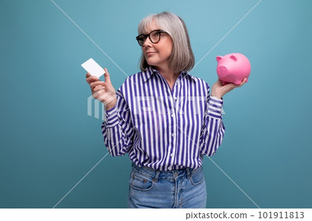 pension contribution. middle-aged woman with gray hair holding a piggy bank and a credit card for pension contribution. middle-aged woman with gray hair holding a piggy bank and a credit card for 101911813