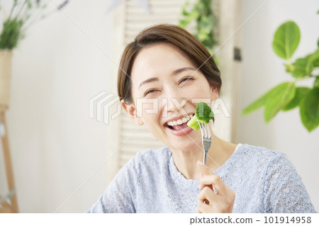 A woman eating broccoli at home looking at the camera 101914958