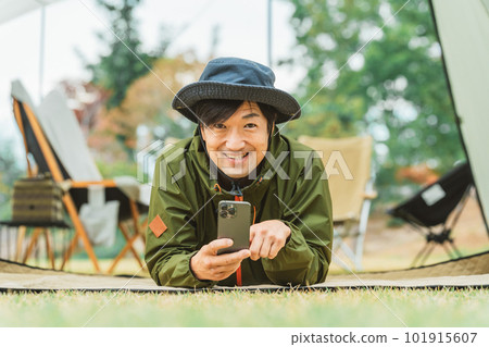 Young asian male camper using smartphone in autumn winter camping outdoors 101915607