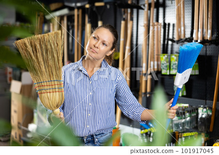 Female farmer choosing broom in gardening store 101917045