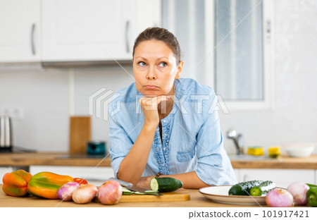 Puzzled female holding face with hand while leaning on the tabletop with vegetables Puzzled female holding face with hand while leaning on the tabletop with vegetables 101917421