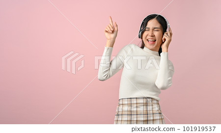 Happy young female listening to music with her headphone, on pink isolated background. Happy young female listening to music with her headphone, on pink isolated background. 101919537
