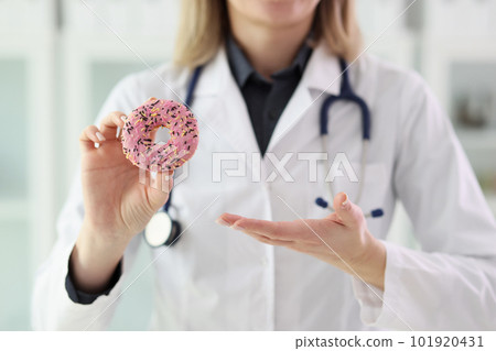 Nutritionist holds fresh donut with pink icing in hand 101920431
