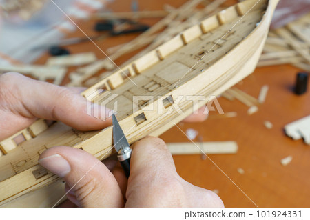 Hands man cutting out details for ship model with clerical knife from plywood. Process of building toy ship, handicraft. Hands man cutting out details for ship model with clerical knife from plywood. Process of building toy ship, handicraft. 101924331